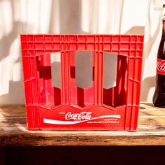 a coca - cola crate sitting on top of a wooden table next to a bottle