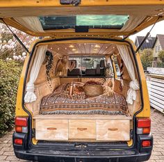 the back end of a yellow van with an open trunk and bedspread on it