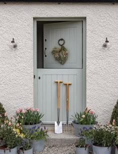 the front door of a white house with flowers and gardening tools