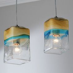 two glass lights hanging from a ceiling in a room with white walls and blue water