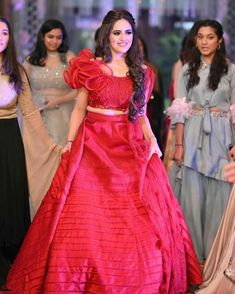 a woman in a red dress standing next to other women wearing long skirts and dresses