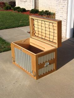 an open box sitting on the sidewalk in front of a brick building with grass and bushes