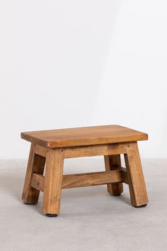 a small wooden bench sitting on top of a cement floor next to a white wall