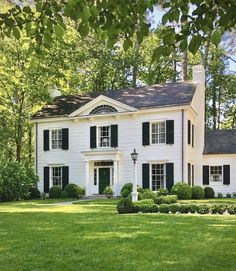 a large white house with black shutters on the front and side windows, surrounded by lush green grass