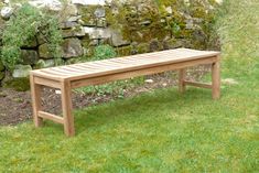 a wooden bench sitting on top of a lush green grass covered park area next to a stone wall