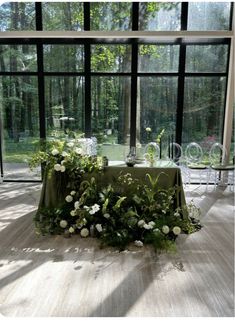 a table with flowers and greenery in front of large windows