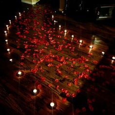 many candles are lit on the floor with red flowers floating in the air and scattered around them