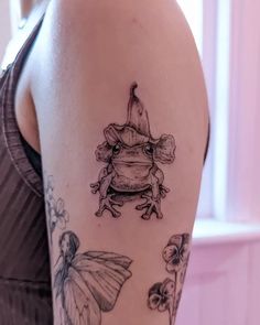 a woman's arm with tattoos on it, including a frog and flowers in the background