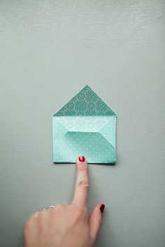 a woman's finger pointing at an origami envelope on the wall with polka dots