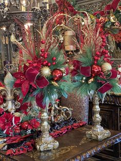 two vases filled with red flowers and greenery on top of a wooden table