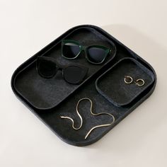 two pairs of sunglasses in a black tray with gold chain and earring clips on it