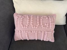 a pink crocheted pillow sitting on top of a couch next to a white pillow