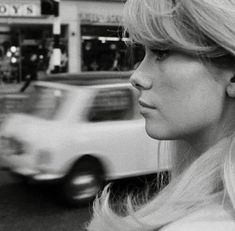 a black and white photo of a woman on the street with cars in the background