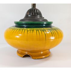 a yellow and green vase sitting on top of a white table next to a lamp