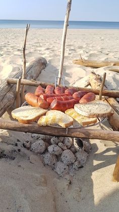 hotdogs and buns are on the beach with sticks in front of them