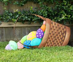 a basket filled with colorfully painted eggs sitting in the grass next to a fence