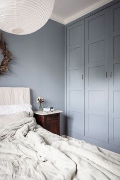 a white bed sitting under a round light fixture in a bedroom next to blue cupboards