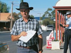 two police officers standing on the street with papers in their hands and one man wearing a cowboy hat