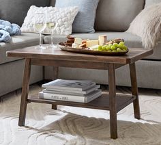 a coffee table with cheese, grapes and bread on it in front of a couch