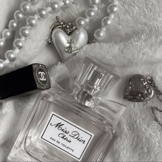 a bottle of perfume sitting on top of a white blanket next to pearls and necklaces