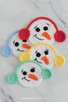 four crocheted snowman coasters with faces on them, sitting on a marble surface