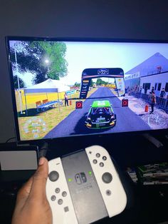 a person holding a nintendo wii game controller in front of a tv screen with cars on it