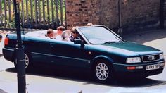 four people in a green convertible car on the street