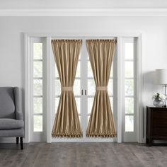 a living room with white walls and wooden flooring, two windows covered in beige drapes