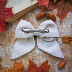 a white bow tie sitting on top of a table next to leaves and an open book