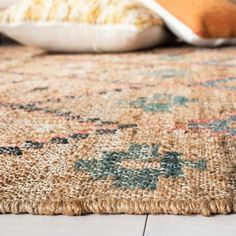 a close up of a rug on the floor with pillows in the background and one pillow laying on top of it