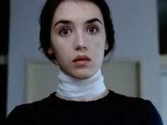 a woman with dark hair and blue eyes wearing a white turtle neck sweater looking at the camera