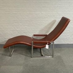 a brown leather chaise lounge chair sitting in front of a white brick wall with a price tag on it