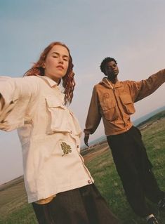 two people standing in the grass with their arms out and one person pointing at something