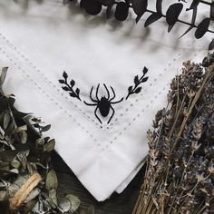 a white napkin with a black spider embroidered on it next to dried flowers and leaves