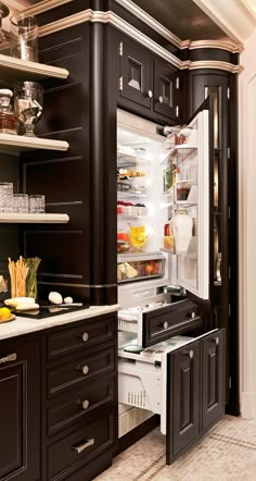 an open refrigerator in a kitchen with black cabinets and white trim on the door handles