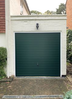 a green garage door in front of a white brick building