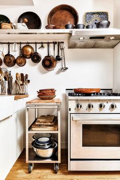 a stove top oven sitting inside of a kitchen next to pots and pans on shelves