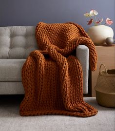 an orange knitted blanket sitting on top of a couch next to a white chair