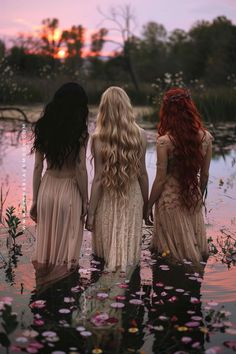 three beautiful women standing in the water at sunset with long hair and flowing dress on