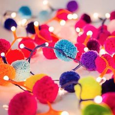 colorful pom - poms and string lights on a white surface with blurry lights in the background