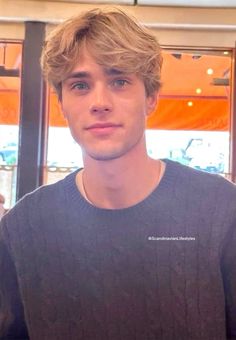 a young man with blonde hair is looking at the camera while wearing a gray sweater