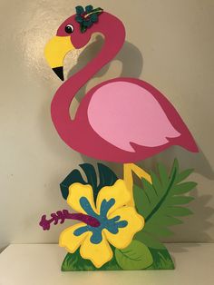 a pink flamingo standing on top of a lush green leafy plant next to a white wall