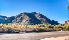 an empty street in the desert with mountains in the backgrouds and trees on either side