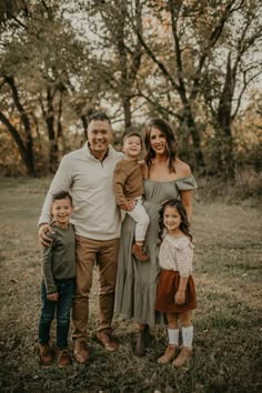 a family posing for a photo in the grass with trees behind them and one man holding his two children