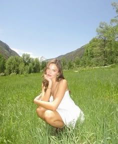 a woman kneeling down in the grass with her hand on her face and looking at the camera