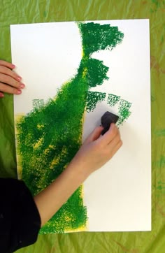 a woman is painting green trees on white paper