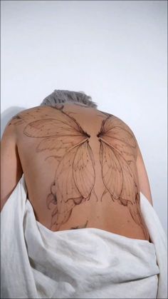 the back of a person with a butterfly tattoo on their upper body and shoulder, wrapped in a white towel