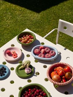 bowls of fruit and vegetables sit on an outdoor table in the grass, ready to be eaten