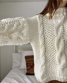 a woman is wearing a white sweater and standing in front of a bed