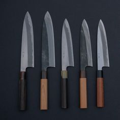 five knives are lined up next to each other on a black surface with wooden handles